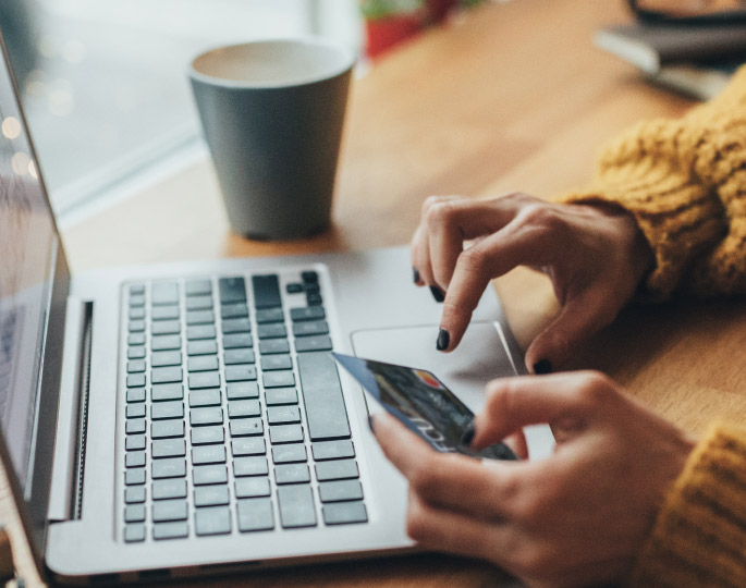 Woman holding her credit card in one hand and typing on her computer with the other.