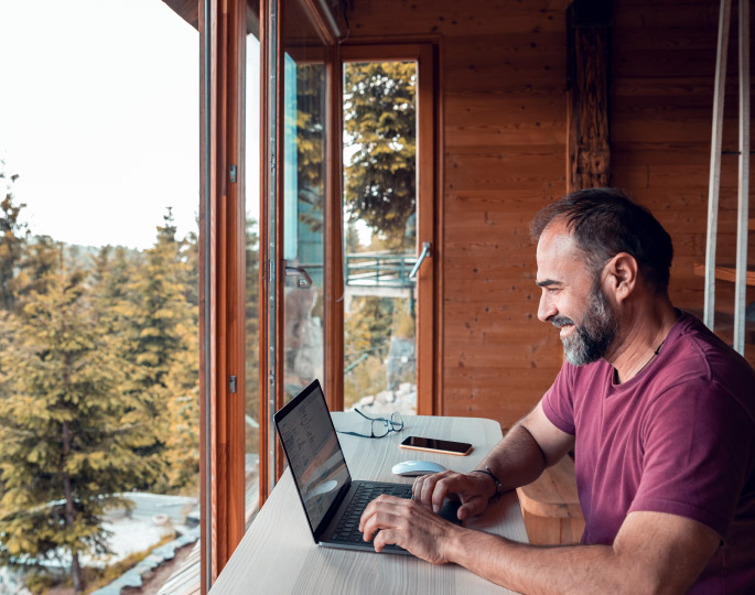Man on his computer while sitting in a cabin with beautiful mountain views.