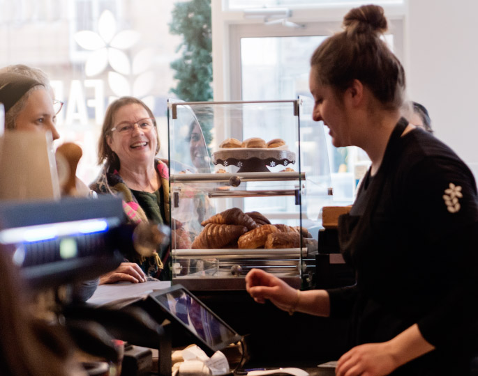 A woman working behind a cafe register, helping customers.