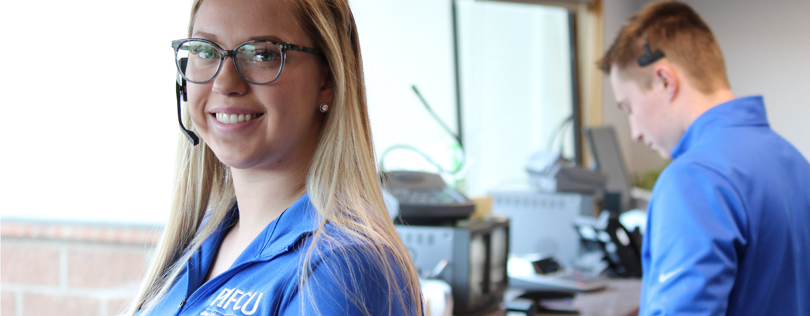 Woman smiling in P1FCU polo while working with headset on