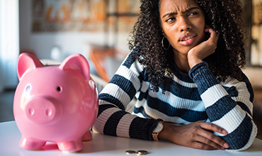 Person looking confused while sitting in front of piggy bank