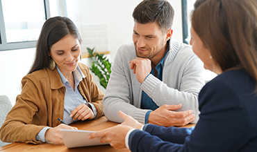 Couple sitting in office signing documents with financial worker