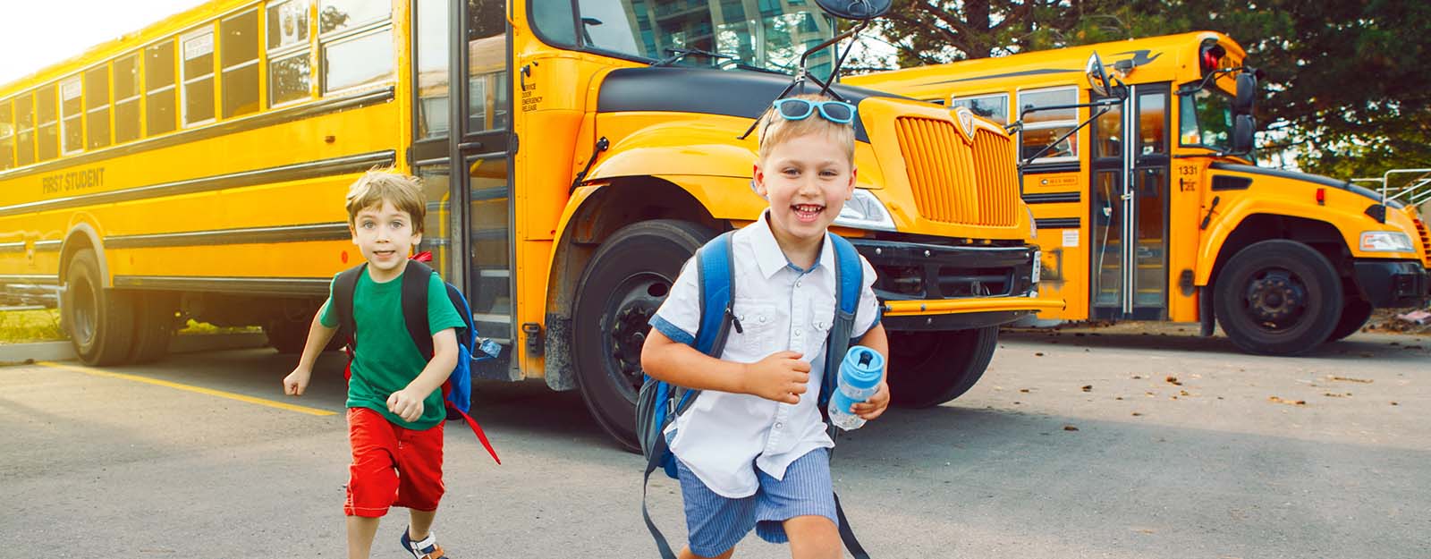 Kids with backpacks smiling while running off school bus