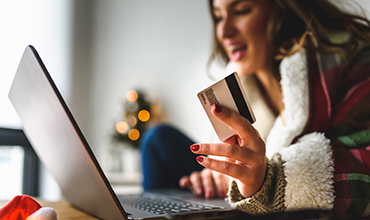 Woman in holiday rob smiling while purchasing items on laptop