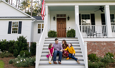 Family sits together on steps of home.