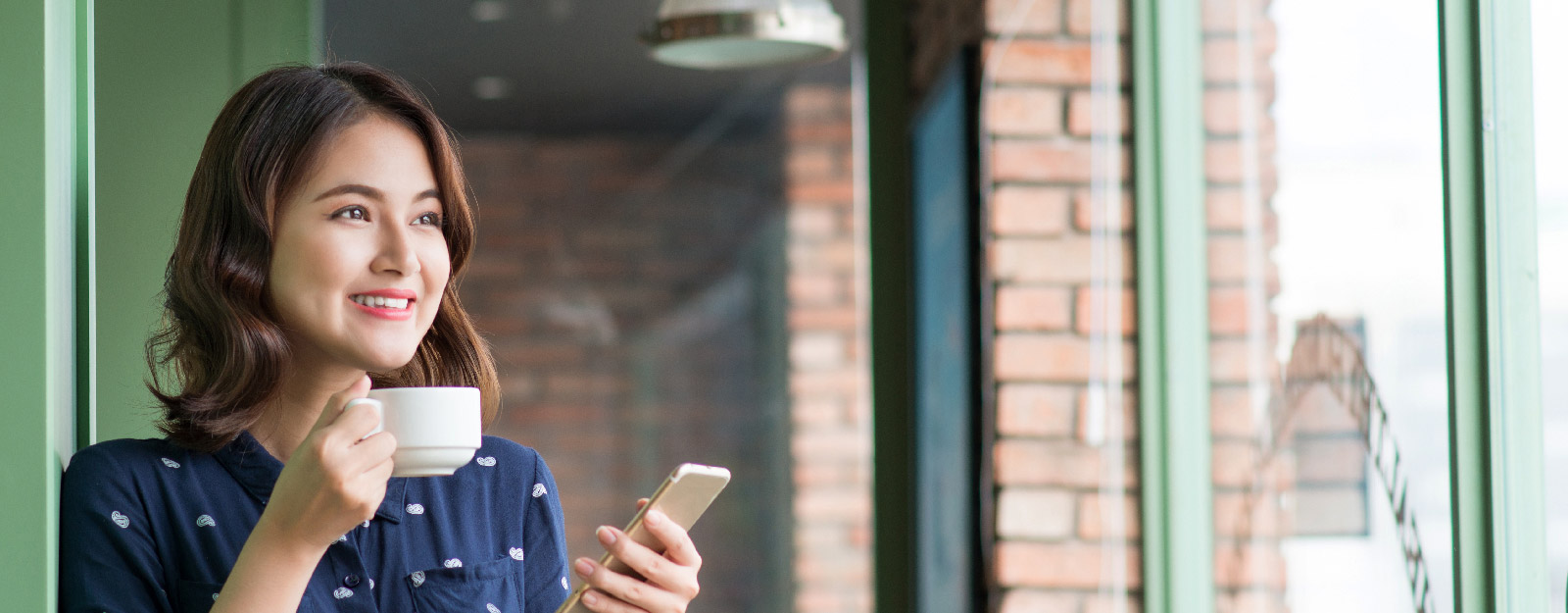 Woman smiling while drinking coffee and holding smart phone