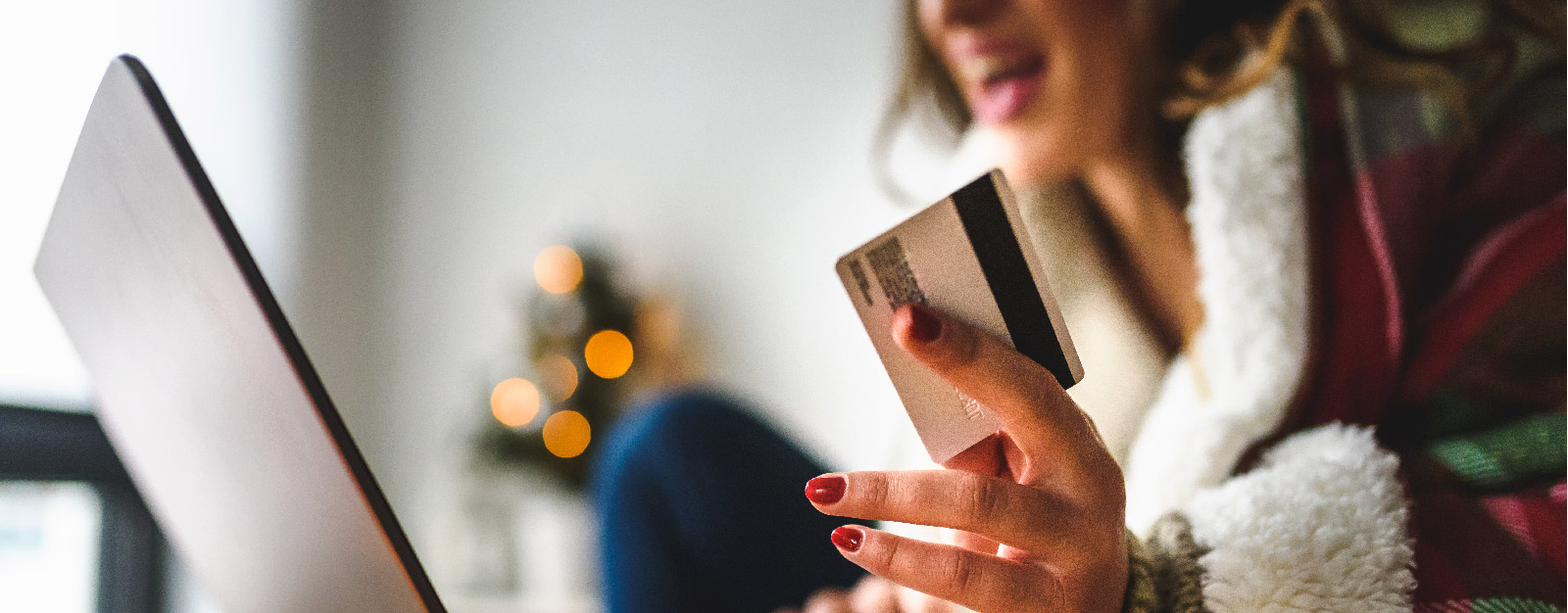 Woman in santa jacket smiling while holding a credit card in front of a laptop